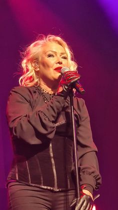 a woman standing in front of a microphone with her hand on her hip and wearing black gloves