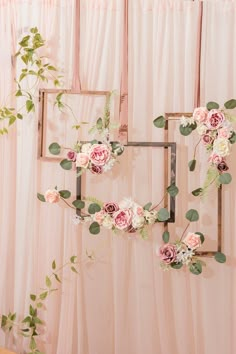 an arrangement of flowers and greenery hangs on the wall in front of a pink backdrop