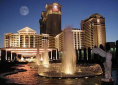 the fountains are lit up at night in front of hotel and casino buildings with full moon behind them