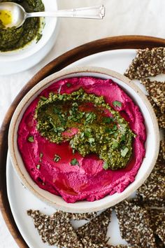 a bowl of beet hummus next to crackers on a plate