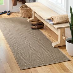 a wooden bench sitting on top of a hard wood floor next to a rug and potted plant