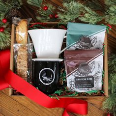 a box filled with coffee, cookies and other items next to a red ribbon on a wooden table