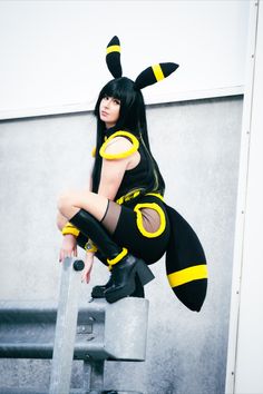 a woman dressed in black and yellow is posing on a metal pole with her legs crossed