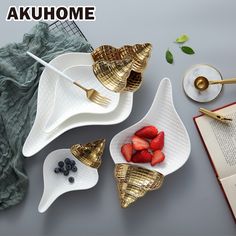 three white dishes with gold spoons and strawberries in them, next to an open book