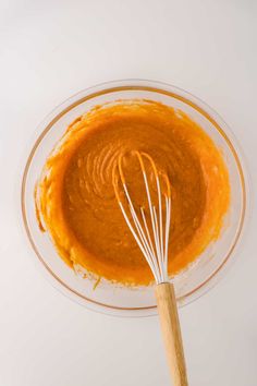 an orange sauce in a glass bowl with a wooden whisk on the side