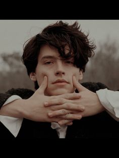 a young man with his hands on his chest looking at the camera while wearing a black jacket and white shirt