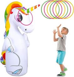 a young boy standing next to an inflatable unicorn with rings around his neck