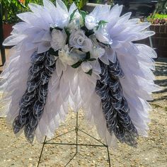 a bouquet of white flowers and feathers on a stand in front of some plants outside