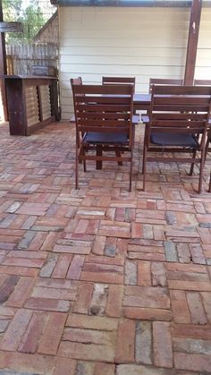 the patio is made out of bricks and has wooden chairs on each side, along with a fire pit