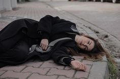 a woman laying on the ground with her head down and eyes closed, wearing a black coat