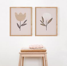 two framed art pieces hang on the wall next to a stool with a pillow in front of it