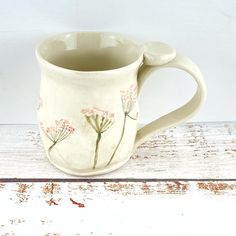 a white coffee mug with pink flowers painted on the outside and inside is sitting on a wooden surface