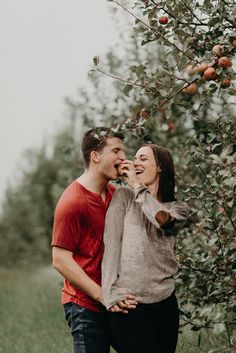 a man and woman standing next to each other in front of an apple tree eating apples