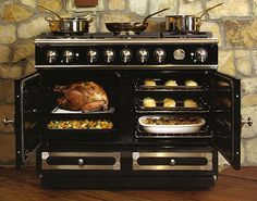 an oven with two turkeys and other food items in front of it on a wooden table