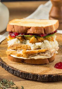 a sandwich with meat, cheese and cranberry sauce on a wooden cutting board