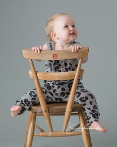 a baby sitting in a wooden chair with her legs crossed and looking up at the camera