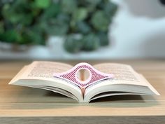 an open book sitting on top of a wooden table next to a potted plant