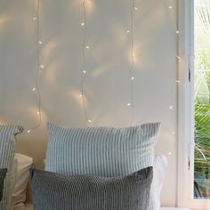 two pillows on a bed with string lights hanging from the headboard