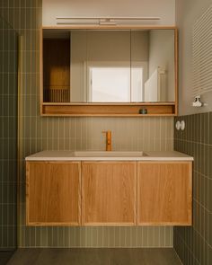 a bathroom with green tiled walls and wooden cabinetry, mirror above the sink area