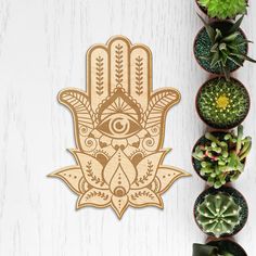 a wooden hamsa hanging on the wall next to succulents