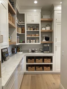 a kitchen with white cabinets and lots of shelves filled with baskets on top of them