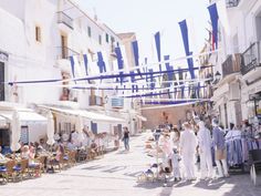 many people are walking down the street in front of some buildings and flags flying above them