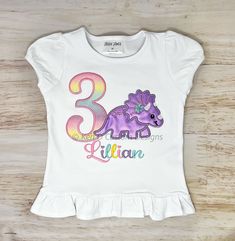 Girl's Triceratops Birthday Shirt, Girl Dinosaur Birthday Shirt, Girl's 3rd Birthday Shirt, Personalized Shirt, Embroidered Shirt, Birthday Shirt, Dinosaur Shirt, Girl Dinosaur, Dinosaur Themed Birthday Party PROCESSING TIME IS 2-3 DAYS + 3-5 days for shipping.  If you need your order sooner please choose a RUSH SHIPPING UPGRADE during checkout.  Shirts are made to order and the design is embroidered, meaning stitched onto the shirt for lasting durability.   Colors may vary slightly due to the screen you are using. Please remember to include NAME & AGE in the personalization section.  PLEASE DOUBLE CHECK YOUR SHIPPING ADDRESS AS I WILL NOT ISSUE A REFUND IF YOUR ITEM IS SHIPPED TO THE WRONG ADDRESS. Summer Dinosaur Print Top For Birthday, Summer Birthday Top With Dinosaur Print, Dinosaur Print Tops For Summer Birthday, Summer Birthday Tops With Dinosaur Print, Pink Dinosaur Print Short Sleeve Top, Birthday Dinosaur Print Short Sleeve Top, Dinosaur Print Short Sleeve Top For Birthday, Cotton Top With Dinosaur Print For Birthday, Cotton Dinosaur Print Top