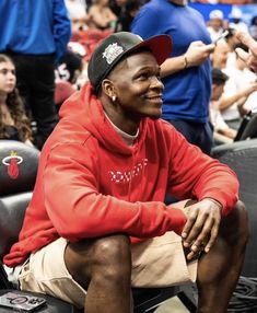 a man in a red hoodie and cap sitting on a bench at a basketball game