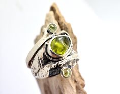 Lovely raw tumbled peridot gemstone and two small round peridots on a freeform leaf band handcrafted from sterling silver The band of the ring it is formed as a leaf and is wrapping the finger ending to small helixes. It is one of a kind ring. The shank of the ring is unusual, textured and have a light oxidation. It is designed on Lesbos island by us Nikiforos and Nelly inspired from walks into the greek nature. The ring is one of a kind and is made in US size 6 ,European 52 and UK M round perid Unique Natural Stone May Birthstone Jewelry, Unique Jewelry With Natural May Birthstones, Unique Natural Stones Jewelry For May Birthstone, Hand Forged Adjustable Oval Jewelry, Unique Gemstone Jewelry For May Birthstone, Unique Peridot Jewelry For May Birthstone, Unique May Birthstone Gemstone Jewelry, Green Peridot Bohemian Jewelry, Hand Forged Nature-inspired Ring