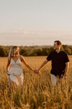 a man and woman holding hands walking through tall grass in the middle of an open field