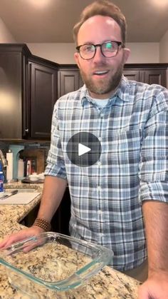 a man standing in front of a kitchen counter holding a glass casserole dish