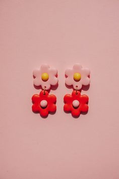 two red and white flower shaped earrings sitting on top of a pink surface next to each other