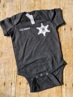 Sheriff Baby Bodysuit ITEM DESCRIPTION This listing is for a PERSONALIZED BABY SHERIFF BODYSUIT. Just provide us with the first initial and last name for the right chest area and the number you would like on the STAR. What a great gift to give a police family to celebrate the birth of a new baby! This police baby shirt would make an ADORABLE birth announcement! Our designs are pressed onto super soft, quality tees. *If you would like this design on a different style shirt, message us and we can Customizable Fitted Onesie For First Birthday, Fitted Onesie With Letter Print For First Birthday, Fitted Letter Print Onesie For First Birthday, Fitted Bodysuit With Name Print For First Birthday, First Birthday Fitted Bodysuit With Letter Print, First Birthday Bodysuit With Letter Print, Police Baby, Police Family, Unisex Baby Clothes