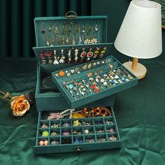 an open jewelry box on a green tablecloth next to a lamp and lampshade