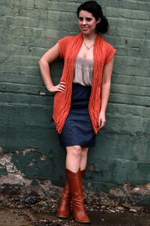 a woman standing in front of a green wall with her hands on her hips and wearing boots