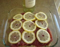 a glass dish filled with sliced up lemons and meat next to a bottle of wine