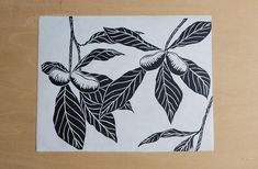 a black and white drawing of leaves on a wooden table with a brown surface in the background