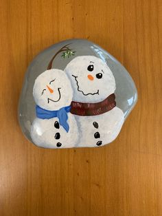 two snowmen sitting on top of a rock