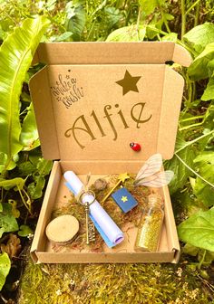 an open cardboard box with some items in it sitting on the ground next to plants