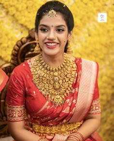 a woman in a red and gold sari sitting on a chair with yellow flowers behind her