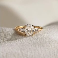 an engagement ring with three pear shaped diamonds on it's side, sitting on a white cloth