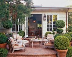 a patio with chairs, tables and potted plants in front of a house that has an open door