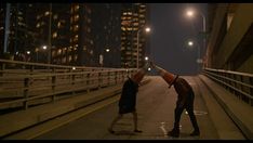 two people standing in the middle of a street at night with their hands on each other's heads