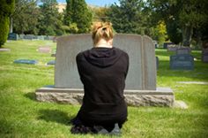 a woman sitting on the ground in front of a headstone with her back turned to the camera