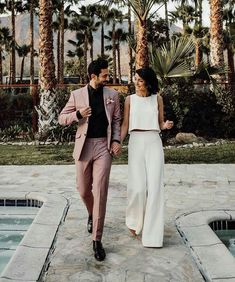 a man and woman holding hands walking next to a pool with palm trees in the background