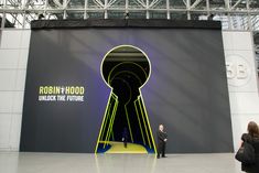 a man standing in front of a giant keyhole sign at an event with the words robin hood unlock the future on it