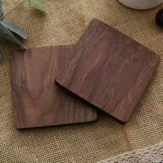 two wooden coasters sitting on top of a table next to a cup and plant