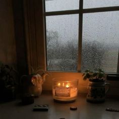 a candle sitting on top of a table next to a window covered in raindrops