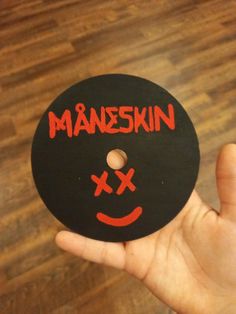 a person holding up a black and red button with the words maheskin written on it