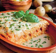 an orange plate topped with lasagna covered in cheese and green leafy garnish